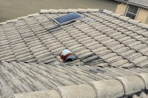 Roof with gray clay tiles, a rectangular skylight, and a rusted vent cap protruding through the tiles.