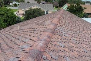 High-angle view of a brown asphalt shingle roof with a long central ridge, overlooking a suburban neighborhood.
