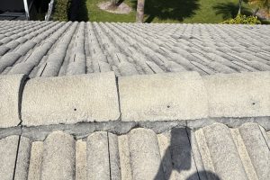 Close-up of a weathered gray tiled roof with a rounded ridge cap and visible cracks, seen from above.
