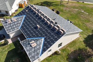 Aerial view of a house roof being reroofed with black underlayment and rows of bricks staged along the ridge for installation.