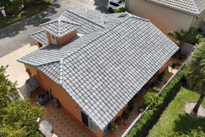 Aerial view of a peach-colored, single-story house with a gray tiled roof, bordered by a tiled patio and green landscaping.