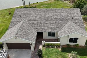 Aerial view of a single-story house with a two-car garage, brick driveway, and manicured front yard beside a lake.