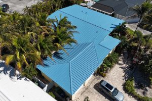 Aerial view of a blue metal-roofed building surrounded by palm trees, with a silver SUV in the stone driveway.