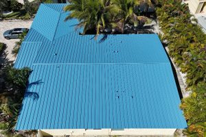 Aerial view of a blue metal roofed building complex with palm trees and a parked car on a driveway.