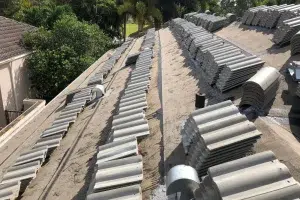 Slate-gray curved roof tiles piled on a sloped rooftop during a roofing project, with trees in the background and scaffolding not visible.