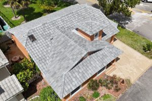 6-Apr 16 2026 01_57pm-DkoC - Monarch Roofing Aerial view of a suburban home with multiple gray tiled roofs, orange-brown walls, and a small front garden area.
