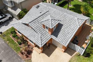 8-Apr 16 2026 01_58pm-K9vY - Monarch Roofing Aerial view of a two-story orange house with a gray tiled roof and a concrete driveway beside a small front garden.